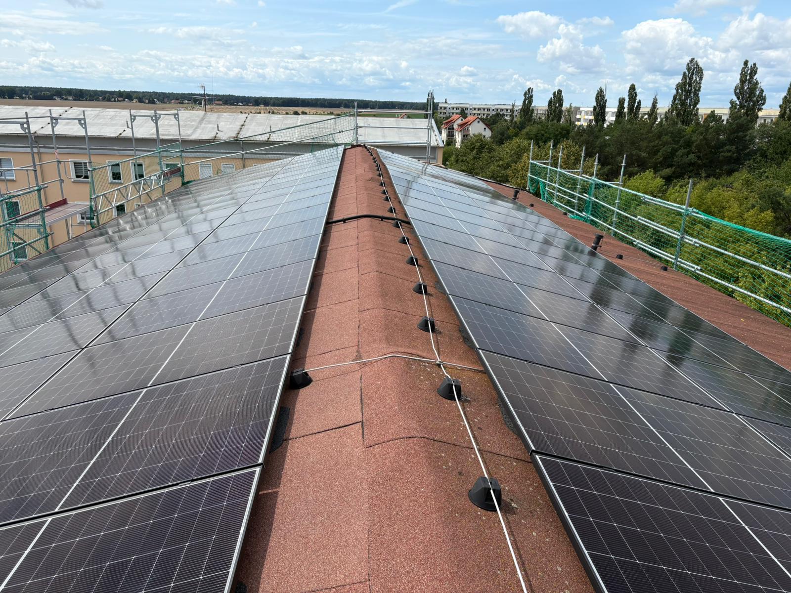 Originalfoto Lausitz R13: PV-Module beidseits des roten Dachfirstes, Wohnbebauung und Landschaft unter blauem Himmel